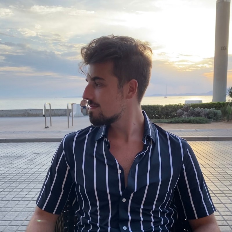 Man in een gestreept overhemd kijkt opzij terwijl hij buiten zit bij zonsondergang aan de kust.