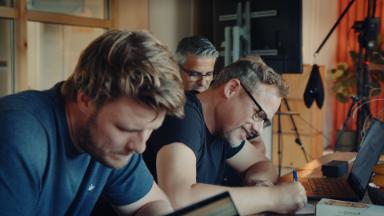 Drie mannen werken geconcentreerd aan een tafel in de Ear Ear podcaststudio in Utrecht.