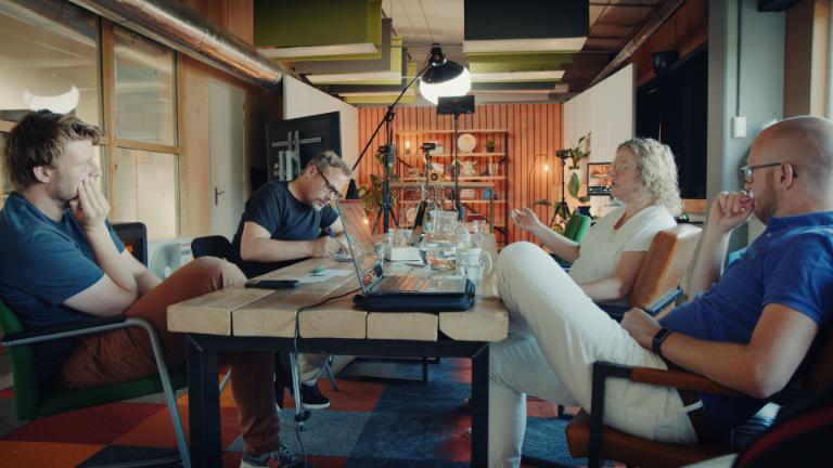 Vier mensen zitten rond een tafel in de Ear Ear podcaststudio in Utrecht tijdens een opnamebespreking.