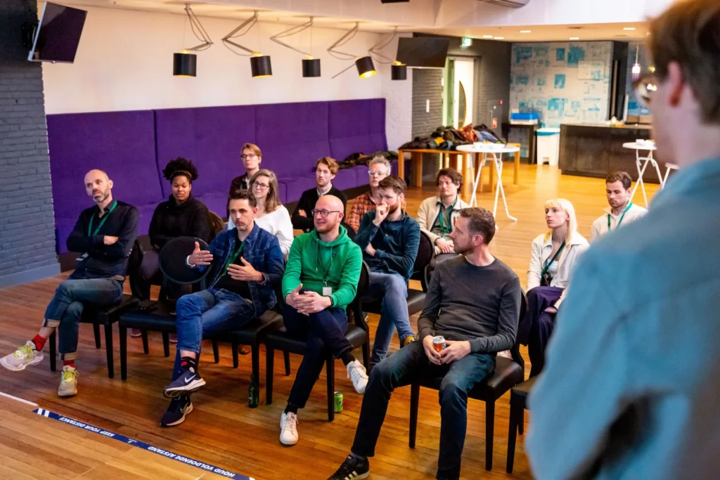 Een groep mensen luistert aandachtig en gaat in gesprek tijdens een bijeenkomst van de EarEar-community in een moderne ruimte.