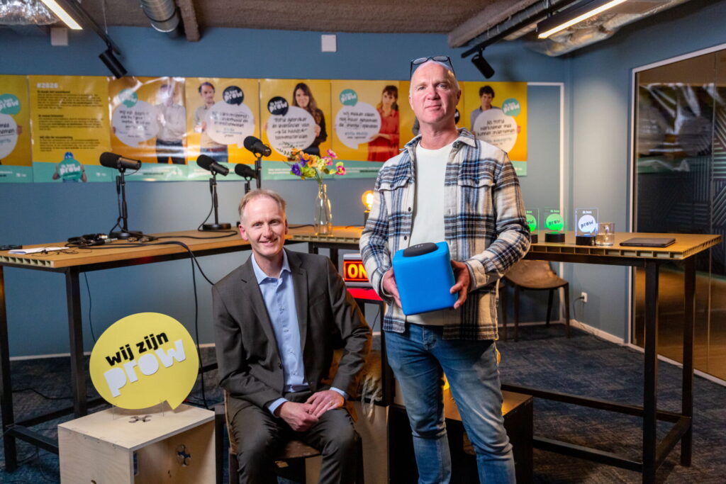 Twee mannen poseren in een podcaststudio met "Wij zijn Prow" branding op de achtergrond.