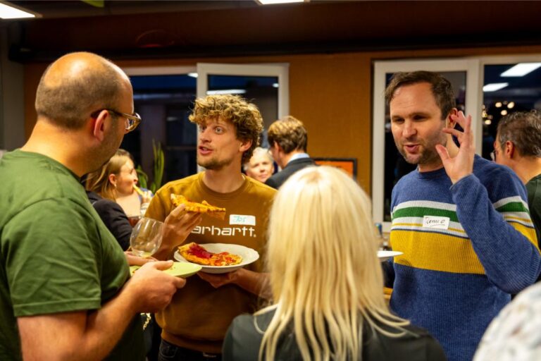 Bezoekers van het All Ears Club-event op 24 oktober voeren een gesprek terwijl ze pizza eten.
