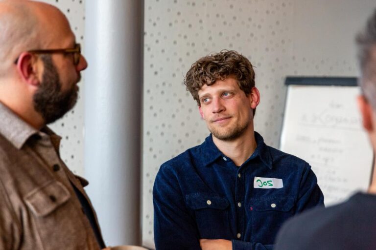 Man met naamsticker 'Jos' luistert aandachtig tijdens een gesprek op het All Ears Club-evenement bij NPO Luister.
