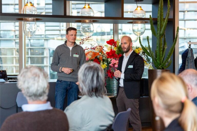 Twee sprekers presenteren voor een groep mensen tijdens het All Ears Club-evenement bij NPO Luister.
