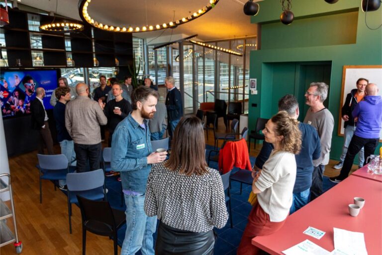 Bezoekers van de All Ears Club bij NPO Luister praten informeel met elkaar in een moderne ontmoetingsruimte.