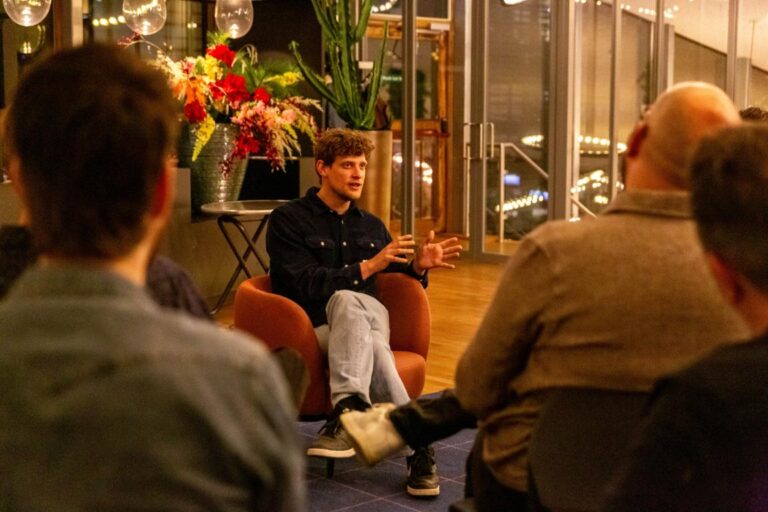 Lars Lensink spreekt gepassioneerd tijdens een All Ears Club-bijeenkomst bij NPO Luister, omringd door aandachtig publiek.