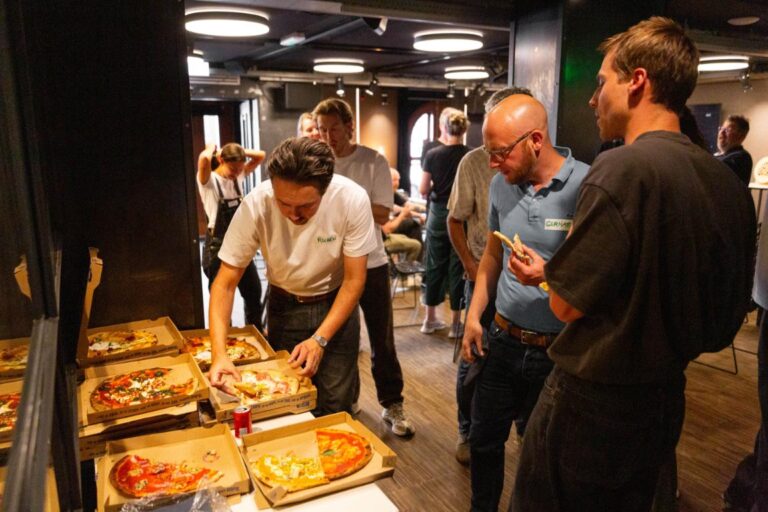 Bezoekers van het All Ears Club-evenement pakken samen pizza uit dozen in een informele setting bij De Stroom.