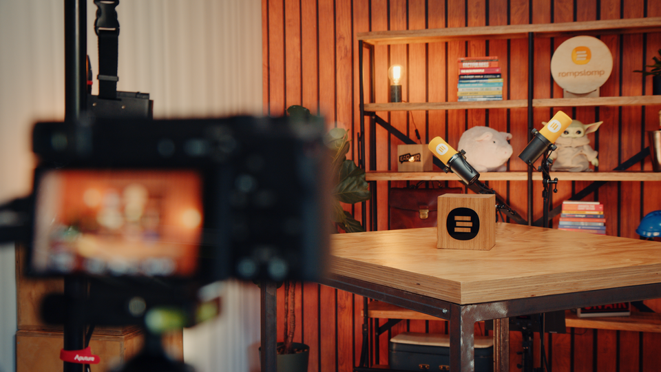 Een professioneel ingerichte podcaststudio met microfoons, een opnametafel en een achtergrond van houten panelen en boekenplanken.