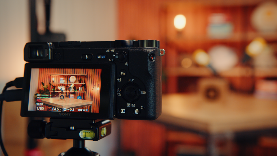 Close-up van een Sony-camera op statief die een houten studio-opstelling met bureau en achtergrondlampen filmt.